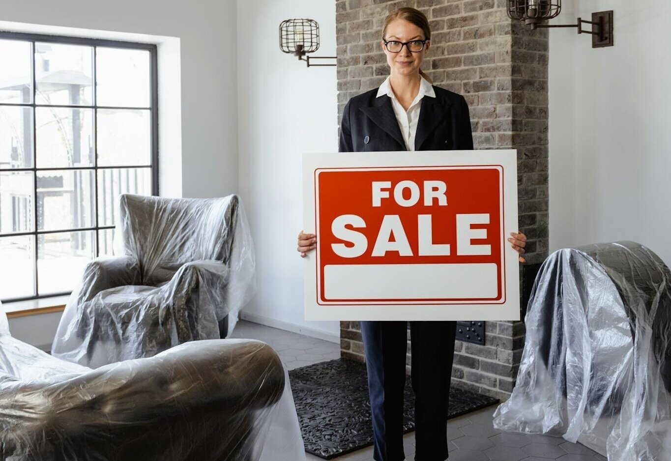 Professional real estate agent holding a 'For Sale' sign in a furnished indoor setting.